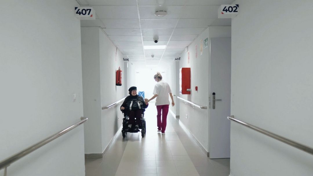 Humanidad en la Residencia de mayores - Trabajadora saluda a residente en pasillo